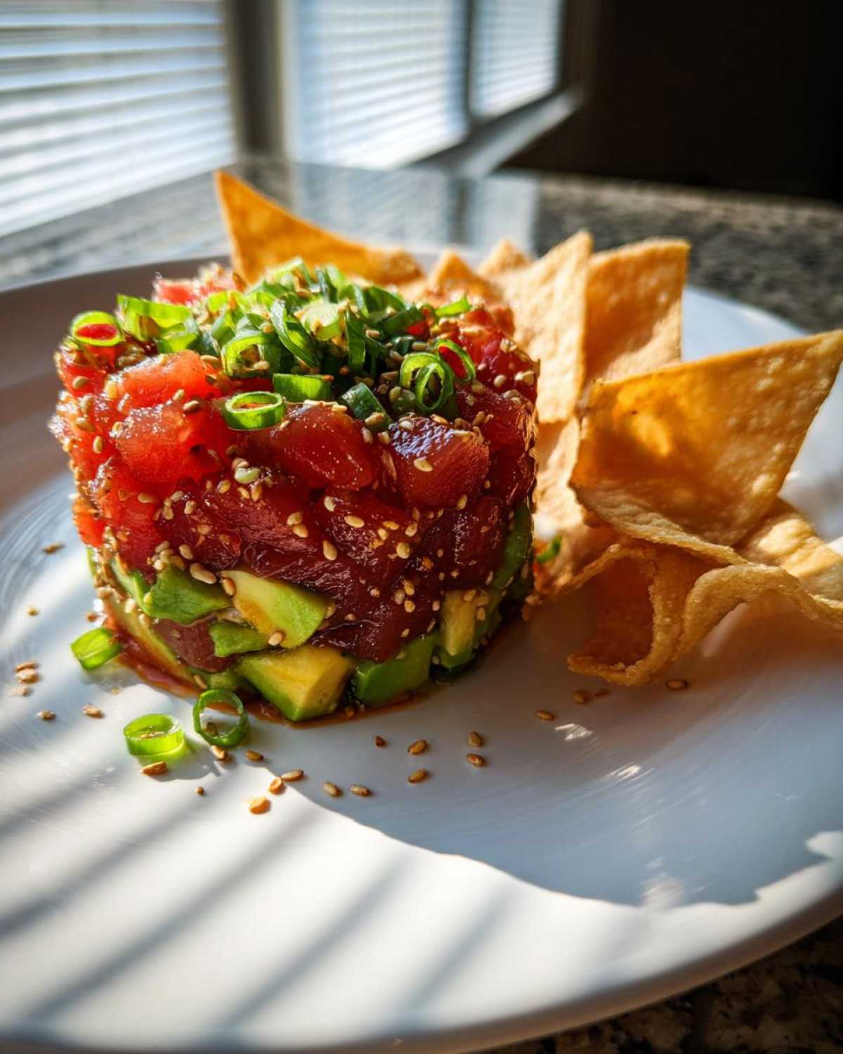 A perfectly molded tower of spicy tuna tartare layered with avocado, topped with green onions and sesame seeds, served with crispy chips.