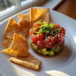 A beautifully plated tower of spicy tuna tartare over avocado, garnished with sesame seeds and jalapeños, served with crispy wonton chips.