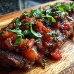 Close-up of a juicy steak pizzaiola covered in rich tomato sauce and fresh basil leaves.