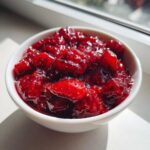 Close-up of chunky strawberry freezer jam with visible seeds, served in a small white bowl near a window.