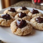 A close-up of several freshly baked peanut butter blossoms rolled in sugar, topped with melted chocolate kisses.