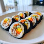 A close-up of several slices of homemade tuna kimbap, showing tuna filling, carrots, cucumber, and yellow pickled radish.