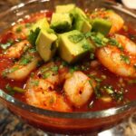 Close-up of a refreshing Mexican shrimp cocktail served in a glass, featuring plump shrimp in red sauce, topped with diced avocado and cilantro.