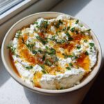 A bowl of creamy whipped ricotta dip drizzled with honey, flaky salt, and fresh thyme.