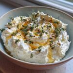 A bowl of fluffy whipped ricotta dip drizzled with honey and topped with fresh thyme leaves.