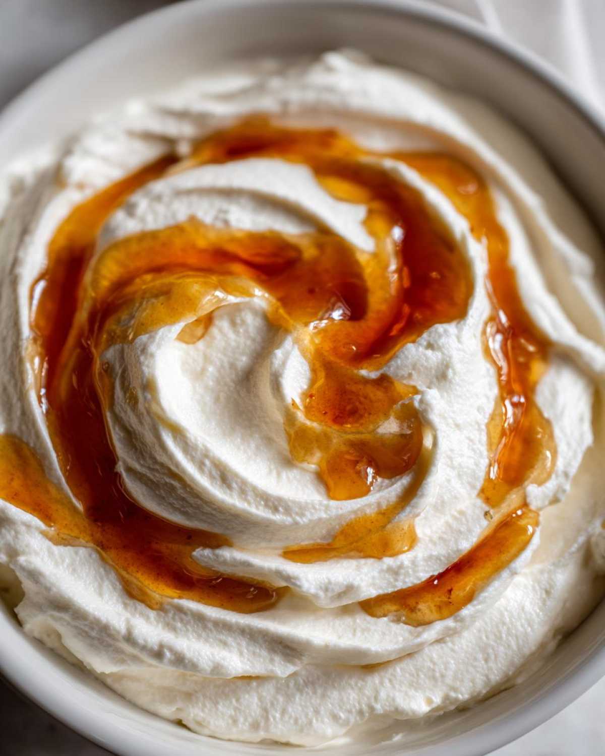 A close-up of creamy, white whipped ricotta dip topped with a beautiful swirl of amber hot honey.
