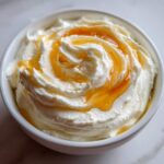Close-up of creamy whipped ricotta dip topped with a swirl of golden hot honey in a white bowl.