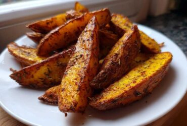 A close-up of crispy, golden-brown seasoned air fryer potato wedges served on a white plate.