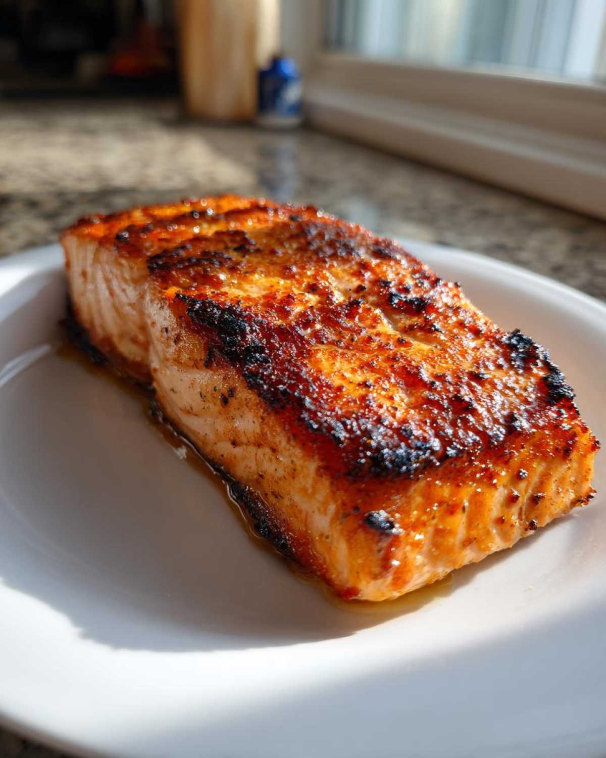 Close-up of a perfectly cooked, caramelized air fryer salmon fillet resting on a white plate.