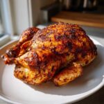 A whole roasted air fryer whole chicken with deeply browned, crispy skin resting on a white plate.