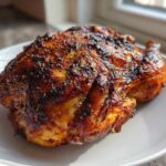 A whole, roasted air fryer whole chicken with crispy, browned skin seasoned with herbs, resting on a white plate.