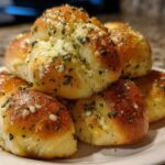 A close-up stack of golden brown, soft breadsticks brushed with garlic butter and sprinkled with parsley.