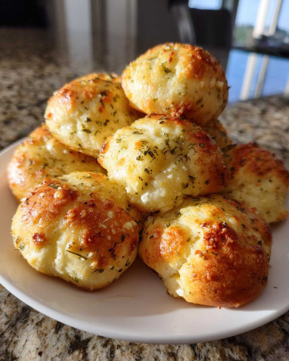 A stack of golden brown, fluffy breadsticks topped with melted cheese and dried herbs on a white plate.