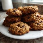 A stack of freshly baked, golden brown breakfast cookie treats loaded with oats and chocolate chips on a white plate.