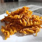 A pile of golden, crispy, shredded baked cheese straws recipe pieces resting on a white plate in bright sunlight.