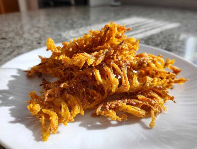 A pile of golden, crispy, shredded baked cheese straws recipe pieces resting on a white plate in bright sunlight.