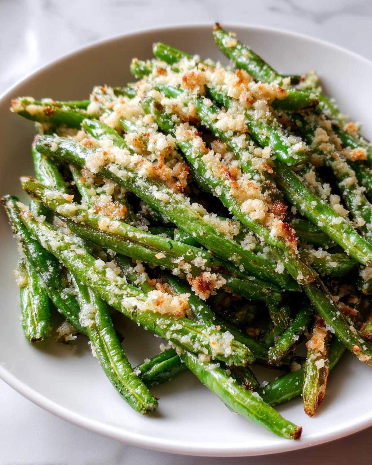 Close-up of bright green beans topped with crispy breadcrumbs served in a white bowl.