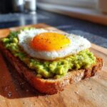 Close-up of delicious avocado toast topped with a sunny-side-up fried egg, seasoned with pepper.