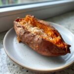 A close-up of a fluffy baked sweet potatoes split open and topped generously with coarse sea salt.