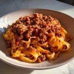 A close-up of fresh tagliatelle pasta generously topped with rich bolognese sauce and grated Parmesan cheese.