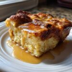 A square slice of moist bread pudding topped with glossy caramel sauce served on a white plate.