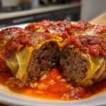 A close-up view of delicious cabbage rolls cut open to show the ground meat and rice filling, smothered in rich tomato sauce.