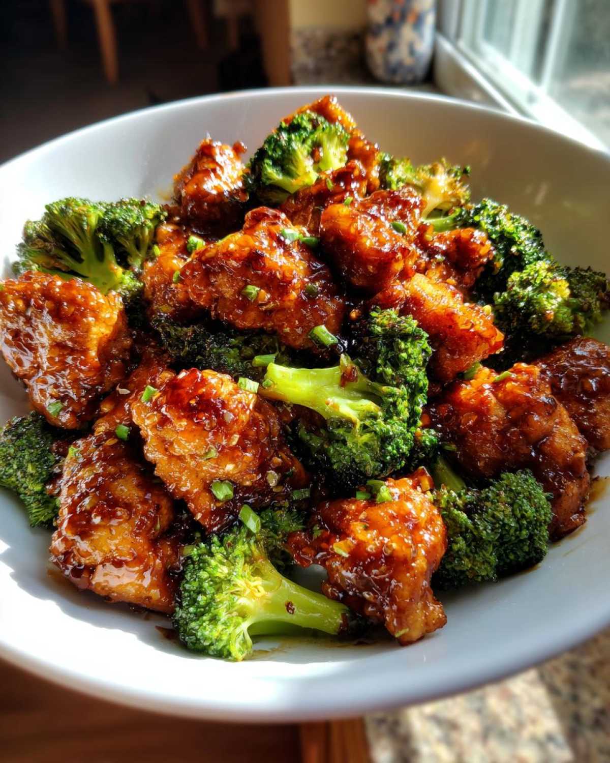Close-up of saucy chicken and bright green broccoli florets in a white bowl, featuring the amazing chicken and broccoli recipe.