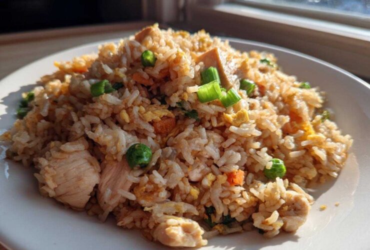 A close-up of a generous serving of amazing chicken fried rice with visible pieces of chicken, peas, carrots, and green onion garnish.