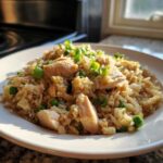 A close-up of a white plate piled high with amazing chicken fried rice, featuring chunks of chicken and topped with fresh green onions.