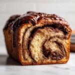 Close-up of a freshly baked chocolate babka showing rich, dark chocolate swirls inside and glossy chocolate glaze on top.