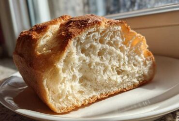 A cross-section of homemade french bread showing the airy interior crumb and golden crust, sitting on a white plate.