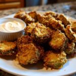 A plate piled high with crispy, golden brown Fried Pickles served alongside a small ramekin of creamy dipping sauce.