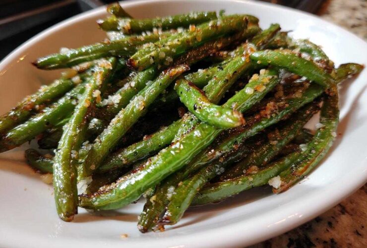 Close-up of bright green beans seasoned with coarse salt and spices served in a white bowl.