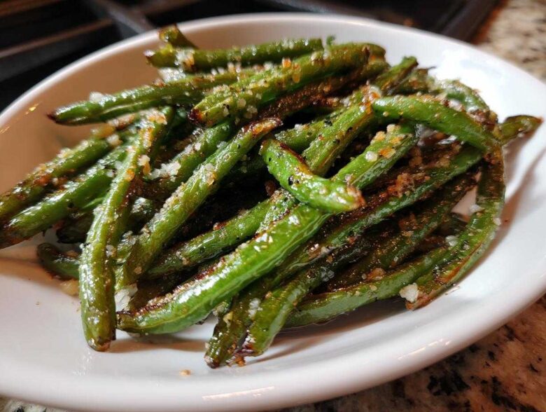 Close-up of bright green beans seasoned with coarse salt and spices served in a white bowl.