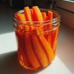 Close-up of bright orange pickled carrots sticks submerged in brine inside a clear glass jar.