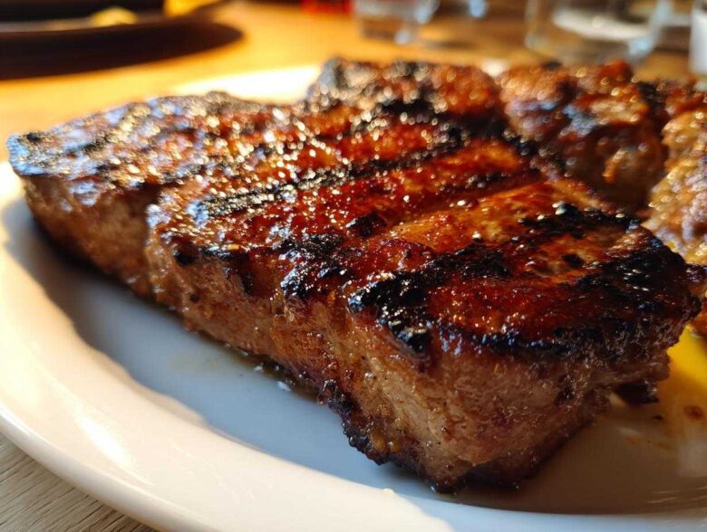 Close-up of a thick, juicy, grilled pork steak recipe with dark char marks and a shiny glaze.