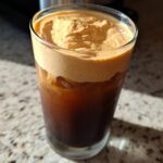 Close-up of a glass filled with ice and cold brew coffee, topped with thick, frothy pumpkin cream cold brew.