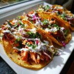 Close-up of three delicious salmon tacos filled with shredded salmon, slaw, and drizzled with white sauce.