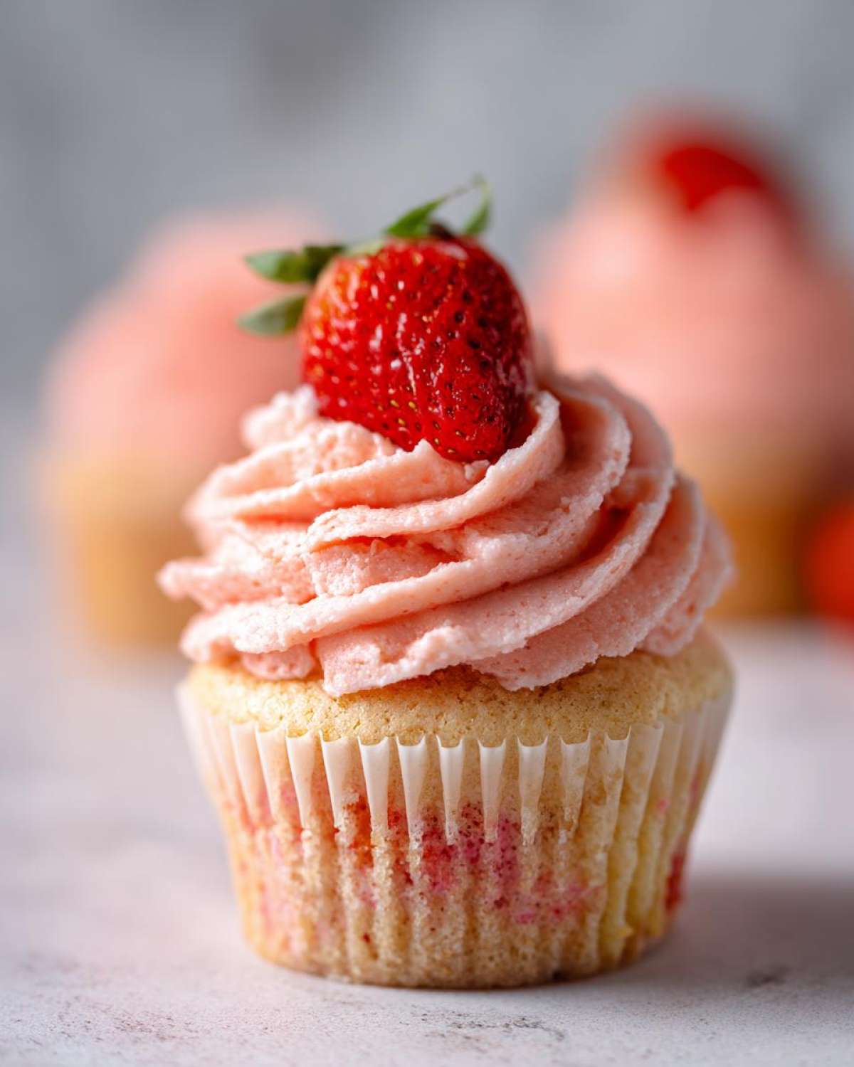 A single, perfectly baked strawberry cupcake topped with pink swirl frosting and a fresh strawberry.