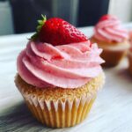 Close-up of a delicious strawberry cupcake topped with pink frosting and a whole fresh strawberry.
