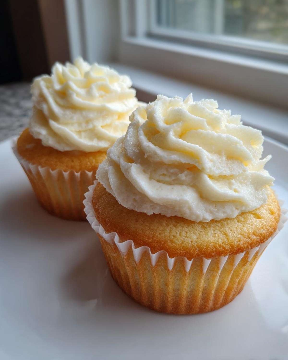 Close-up of two delicious vanilla cupcakes topped with high swirls of white frosting, ready to eat.