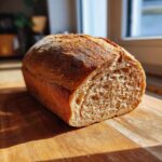 A close-up of a freshly baked whole wheat bread loaf, sliced to show its airy crumb, resting on a wooden board.