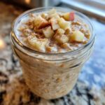 Close-up of apple cinnamon overnight oats in a glass jar, topped with diced apples and cinnamon.
