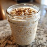 A glass jar filled with creamy apple cinnamon overnight oats, topped with diced apples and a sprinkle of cinnamon.
