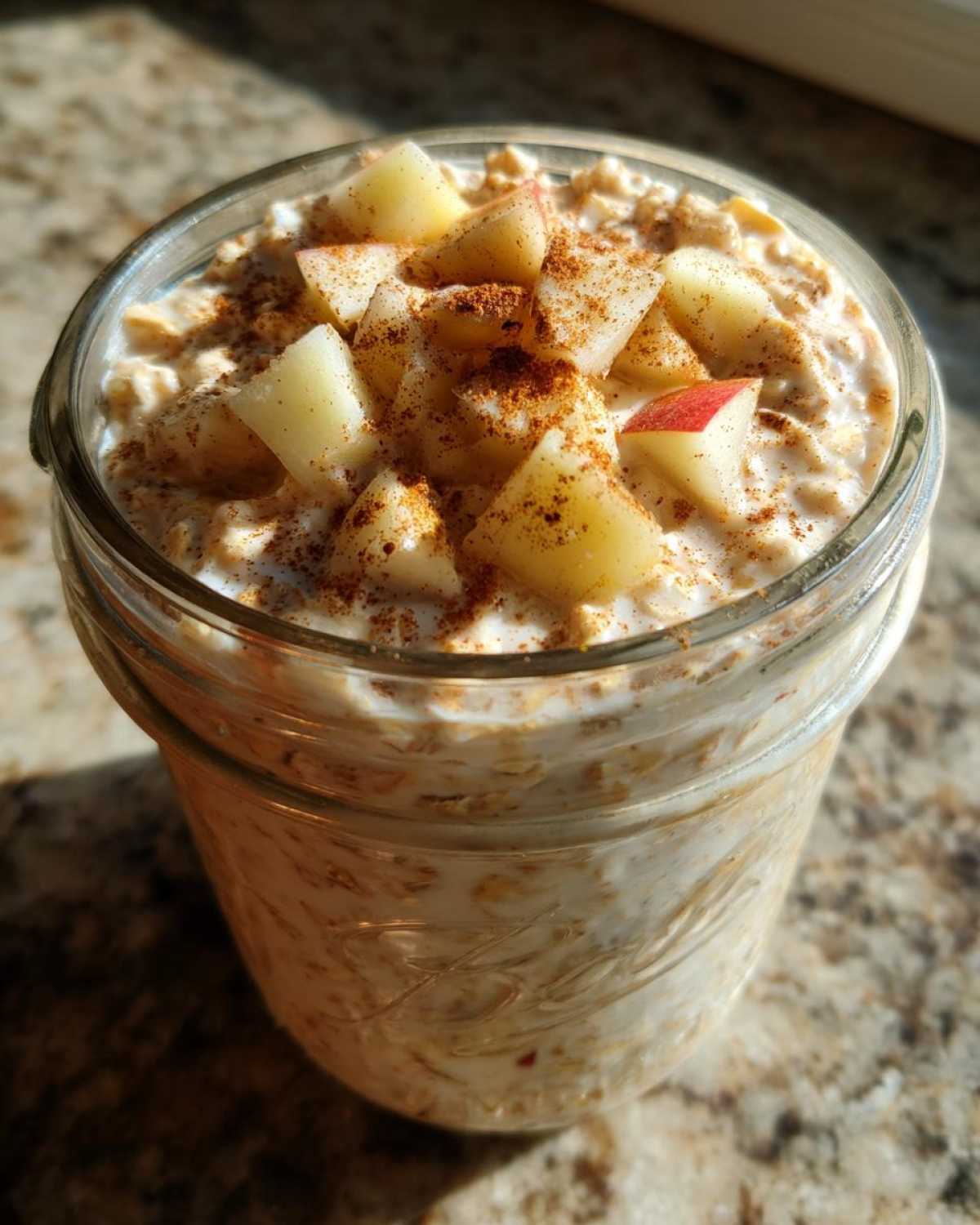 Close-up of apple cinnamon overnight oats in a mason jar, topped with diced apples and cinnamon.
