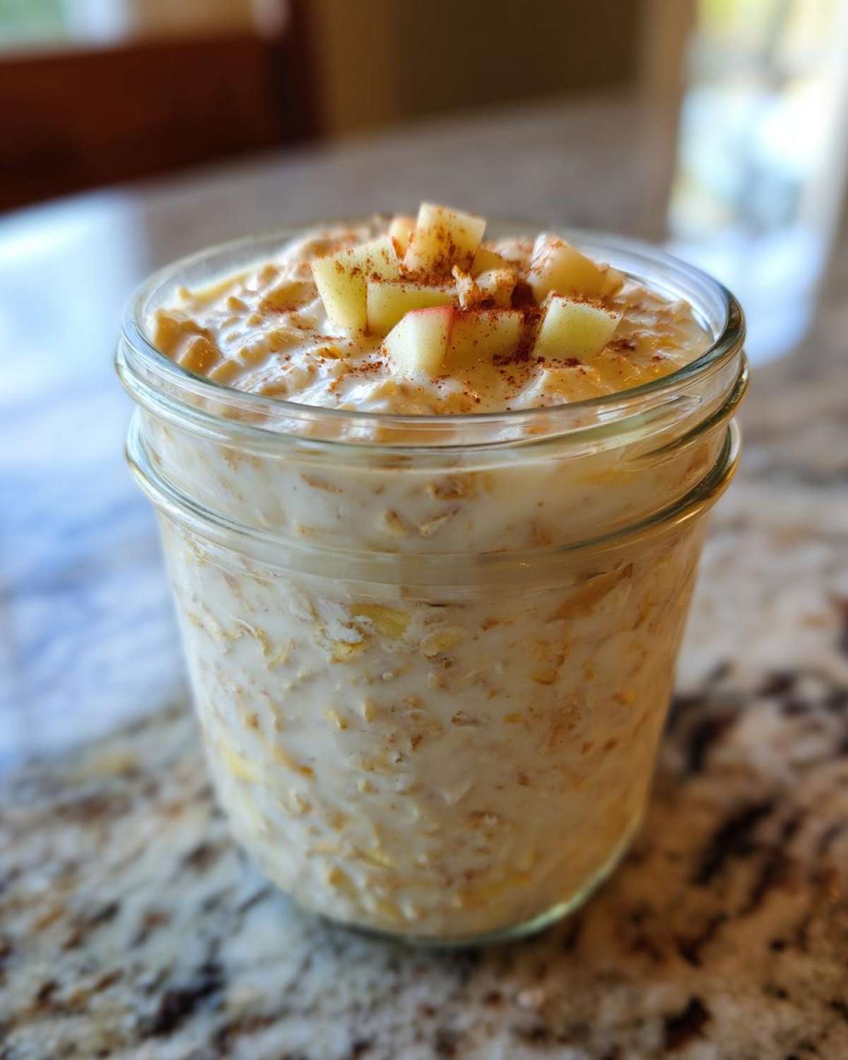 Close-up of apple cinnamon overnight oats in a glass jar, topped with diced apple and cinnamon.