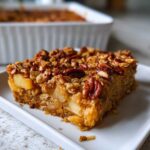 A square slice of apple pecan baked oatmeal served on a white plate, showing chunks of apple inside.