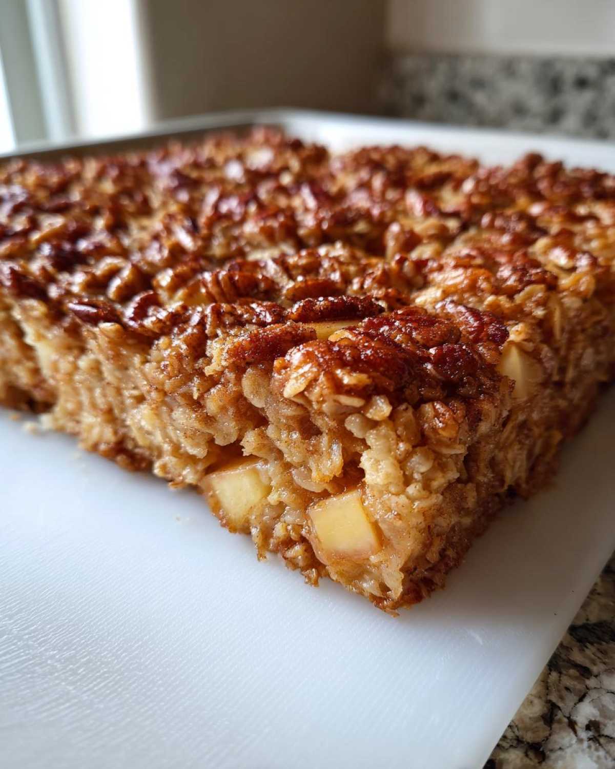 A close-up view of a square slice of apple pecan baked oatmeal showing oats, apple chunks, and a caramelized pecan topping.