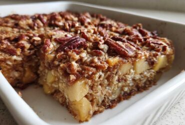 A thick slice of apple pecan baked oatmeal with a crunchy topping, sitting in a white baking dish.