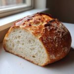 A cross-section of homemade artisan bread showing an open, airy crumb structure and a deeply browned, crackled crust.